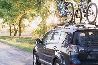 Car parked on a tree-lined road with bicycles mounted on the roof rack during sunny daytime. Car parked on a tree-lined road with bicycles mounted on the roof rack during sunny daytime.