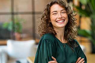 Woman with curly hair wearing a dark green blouse, standing indoors