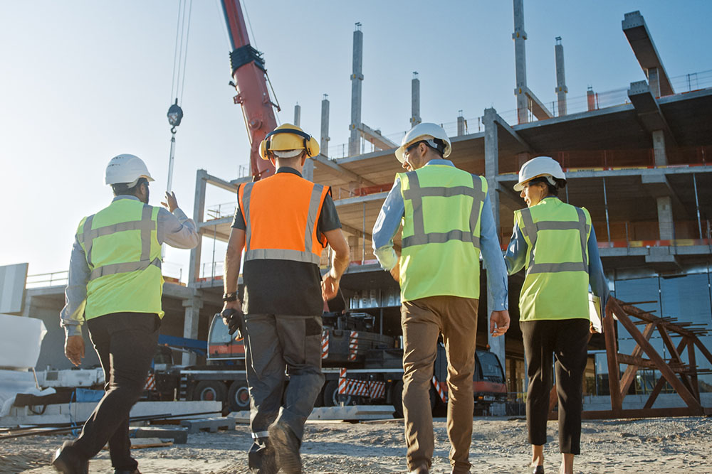 Four construction workers wearing safety vests and helmets walking at a construction