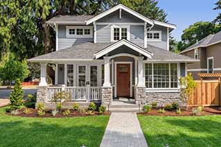 Front view of a two-story gray house with white trim, a covered porch with stone pillars
