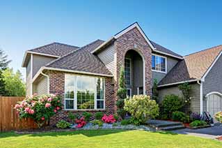 Two-story brick house with large arched window, well-maintained garden with colorful flowers, and green lawn under clear sky Two-story brick house with large arched window, well-maintained garden with colorful flowers, and green lawn under clear sky